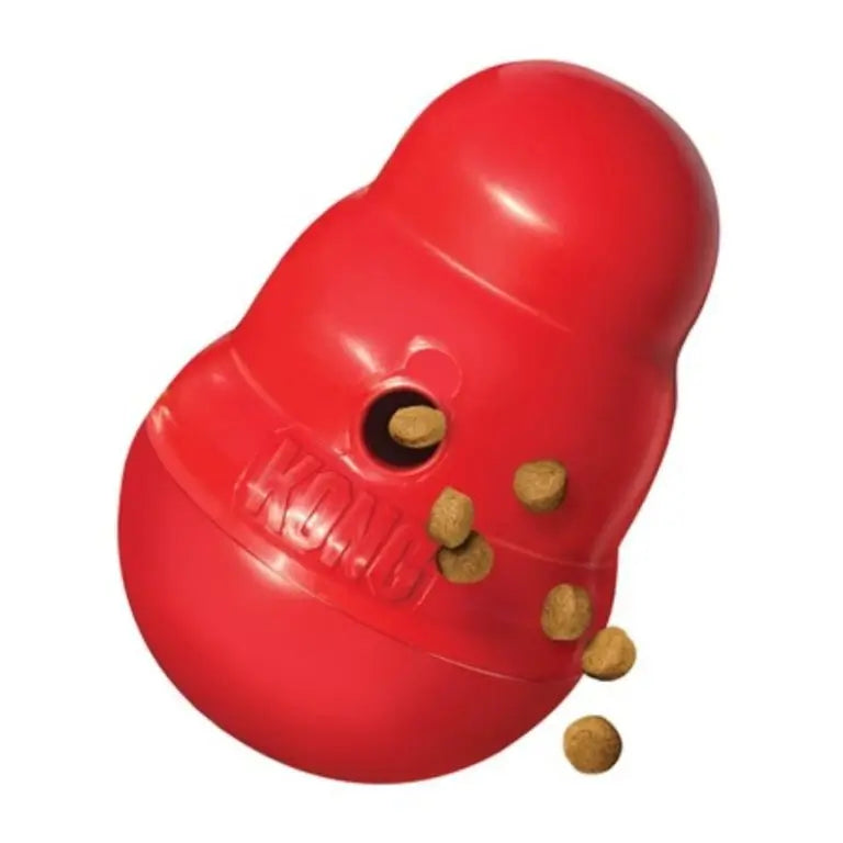 Red KONG Wobbler interactive dog toy tilted on its side with dry kibble dispensing through the treat opening.
